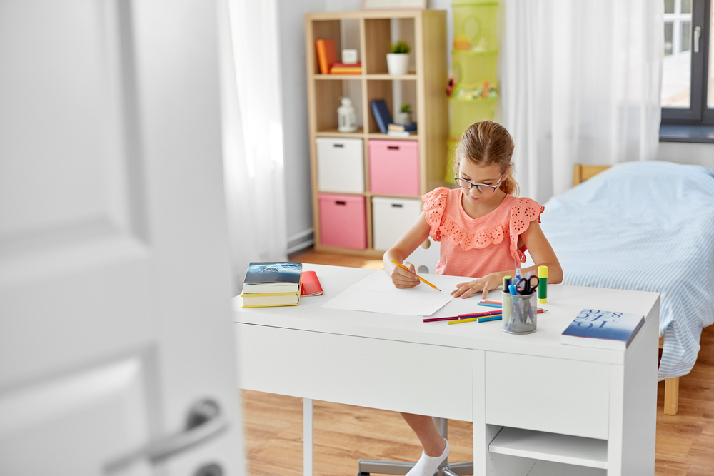 Niña estudiando en un escritorio infantil en su habitación, resaltando la importancia de un espacio propio para el aprendizaje, la creatividad y la organización.